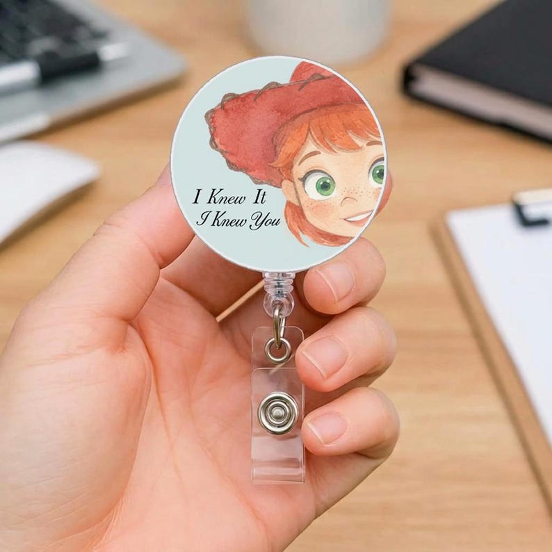 May include: A circular badge reel featuring a watercolor-style illustration of a character with red hair and a red hat, set against a light blue background. The text "I Knew It I Knew You" is printed in black on the left side of the badge.