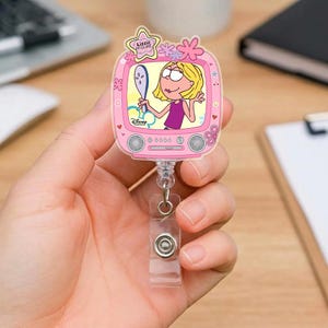 Könnte beinhalten: Ein rosa einziehbarer Ausweis-Rollenhalter mit einem Cartoon-Bild von Lizzie McGuire in einem Fernsehdesign. Die Rolle hat einen transparenten Kunststoffclip und einen Metallschnappverschluss. Auf der Oberseite der Rolle steht der Text "Lizzie McGuire" und das Disney-Branding.