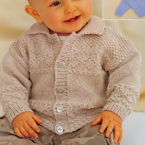 May include: A baby wearing a beige knitted cardigan with a button closure. The cardigan has a collar and a textured pattern. The baby is smiling and sitting on a camouflage patterned fabric.