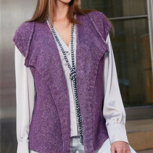 May include: A sleeveless purple knit vest featuring a wide, textured lapel and a ribbed front border. The garment is worn over a light gray long-sleeved button-down shirt, paired with a long necklace of dark gray beads and light gray trousers.
