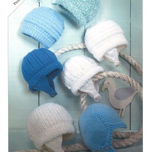 Könnte beinhalten: Sieben gestrickte Baby-Mützen in verschiedenen Blautönen und Weiß. Die Mützen haben Ohrenklappen und einen Knopfverschluss. Die Mützen werden auf einem hellblauen Holzhintergrund mit einem Seil und einer Möwen-Dekoration präsentiert.