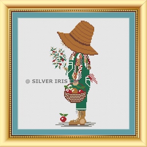 Könnte beinhalten: Kreuzstich-Bild einer Vogelscheuche in einem goldenen Rahmen. Die Vogelscheuche trägt einen braunen Hut und grüne Latzhosen und hält einen Korb mit Äpfeln und Beeren. Das Kunstwerk befindet sich vor einem hellblauen Hintergrund mit dem Text "@ SILVER IRIS CO".