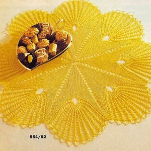 May include: A yellow crocheted doily with a scalloped edge. The doily is laid flat on a white surface and has a heart-shaped plate with chocolates on top.