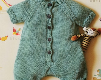 May include: A knitted baby romper in a light green color with a button closure down the front. The romper has short sleeves and a round neckline.