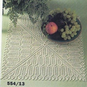 May include: A white crocheted doily with a delicate pattern, featuring a square shape with a central design. The doily is displayed on a green surface with a bowl of fruit on top.