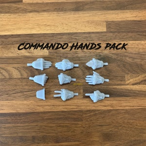 May include: A set of 10 grey plastic 3D printed hands in various poses. The hands are for use with action figures or other miniature models. The set is labelled "COMMAND HANDS PACK".