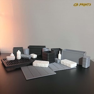 Peut inclure: Une collection de contenants et de boîtes en plastique gris, blanc et noir. Les contenants sont disposés sur une surface grise avec un motif de grille noire. Les contenants sont de différentes tailles et formes. Le texte "CB PRINTS" est visible dans le coin supérieur droit de l'image.