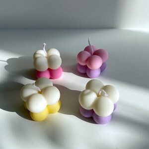 May include: Four small, round, multi-colored candles with a flower-like shape. The candles are white, pink, yellow, and purple.