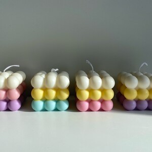 May include: Four colorful bubble candles with three layers of different colors. The top layer is white, the middle layer is yellow, and the bottom layer is a mix of pink and purple.