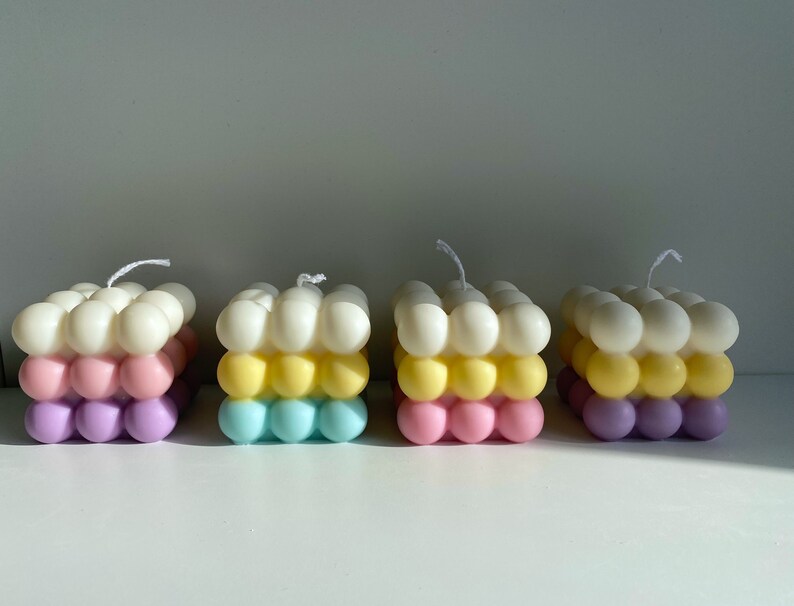 May include: Four colorful bubble candles with three layers of different colors. The top layer is white, the middle layer is yellow, and the bottom layer is a mix of pink and purple.