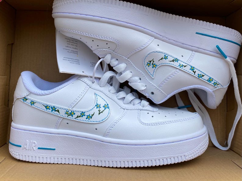 Custom Nike Air Force 1 sneakers featuring a delicate hand-painted floral forget-me-not design on the swoosh, perfect for unique footwear enthusiasts