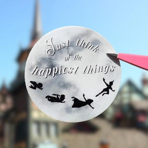 May include: A circular white sticker with a cloudy grey watercolour background featuring the black silhouette of four figures flying. The text "Just think of the happiest things" is printed in a dark, stylised font across the upper portion.