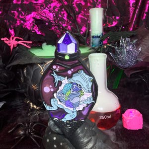 May include: Purple glass bottle with a crystal stopper and a frog inside. The bottle is sitting on a black surface with a green liquid in the background.