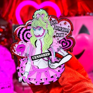 May include: A pink and red enamel pin featuring a cartoon woman with green hair and a pink dress. The pin has the words "FAR FUCKING OUT!" and "CENSORED" on it. The pin is decorated with hearts, bows, and dripping details.