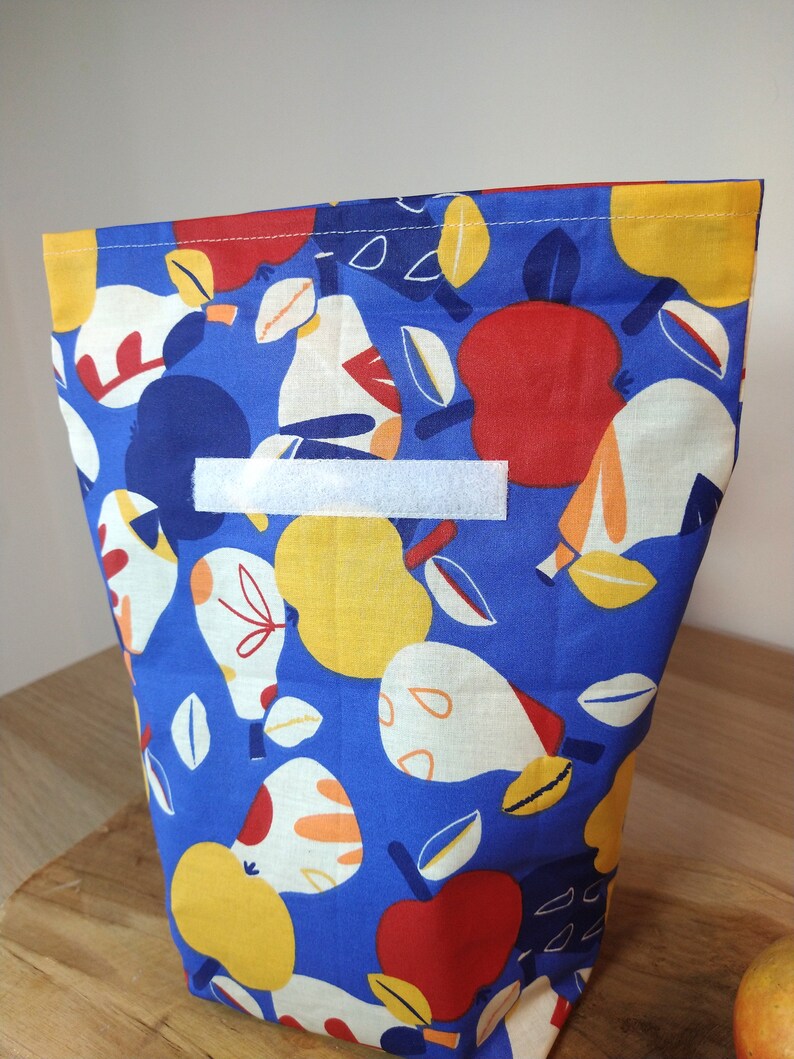May include: A blue fabric reusable bag with a white label and a pattern of red apples, yellow pears, and white leaves.