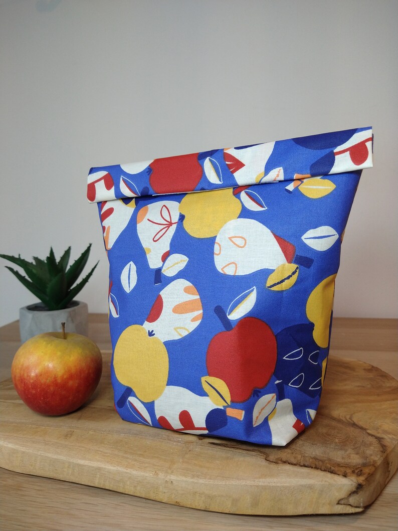May include: A blue fabric lunch bag with a colorful pattern of apples and pears. The bag is folded over at the top and has a white lining.