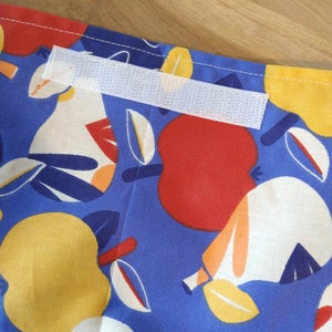 May include: A blue fabric with a white, red, and yellow fruit pattern. A white hook and loop fastener is sewn onto the fabric.
