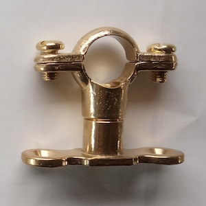 Może przedstawiać: Złota opaska zaciskowa do rur z okrągłym otworem i dwiema śrubami. Zacisk ma podstawę z dwoma zakrzywionymi sekcjami. Metal ma błyszczące wykończenie.