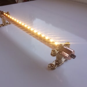 May include: A copper pipe light fixture with a row of warm white LED lights. The fixture is mounted to a wall with two brass brackets.