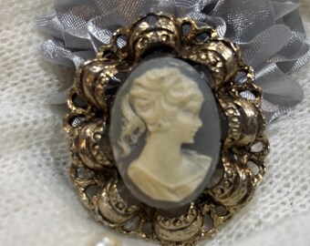 Broche vintage con camafeo, fondo gris y marco dorado.