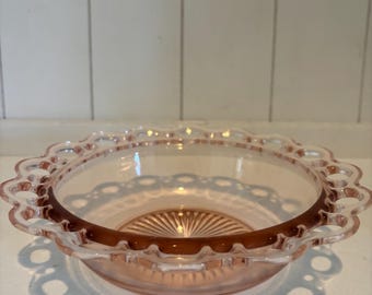 Pode incluir: Uma tigela de vidro rosa com borda ondulada e um padrão decorativo. A tigela tem formato circular com uma borda ligeiramente alargada. A base da tigela tem um design texturizado e canelado. A tigela é provavelmente vintage ou antiga.