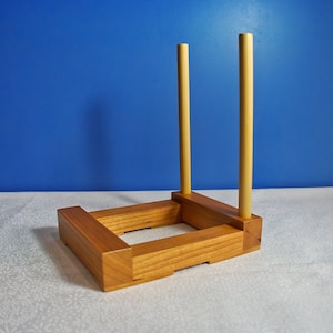 May include: A wooden stand with two upright dowels, designed to hold and display items like plates or platters.