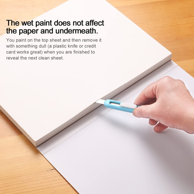 May include: A white pad of paper with a blue utility knife cutting through the top sheet. The text on the pad reads: "The wet paint does not affect the paper and underneath. You paint on the top sheet and then remove it with something dull (a plastic knife or credit card works great) when you are finished to reveal the next clean sheet."