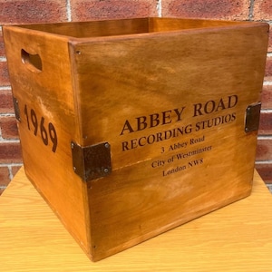 May include: A wooden box with the text "ABBEY ROAD RECORDING STUDIOS" and "1969" printed on it. The box is stained a light brown colour and has metal corner reinforcements.