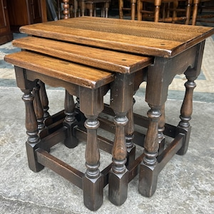 May include: A set of three nested tables crafted from dark brown wood, featuring rectangular tops with visible grain patterns and sturdy legs with turned detailing. The tables are designed to slide underneath one another for compact storage.