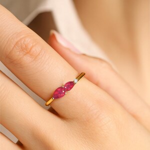 K&ouml;nnte beinhalten: Ein goldener Ring mit zwei markant roten, marquisef&ouml;rmigen Edelsteinen, die nebeneinander gesetzt sind. Zwischen den roten Steinen befindet sich ein kleiner, runder, klarer Edelstein. Der Ring befindet sich an einem Finger.