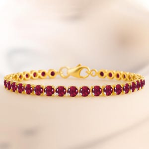 May include: A gold bracelet adorned with a sequence of oval-cut, deep red gemstones. The bracelet has a traditional design with a secure clasp. The gemstones are set in individual gold settings, forming a continuous line of colour.