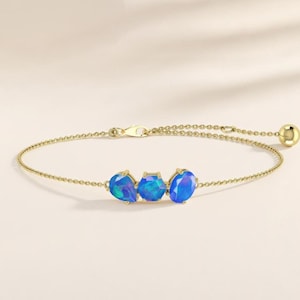 May include: A gold chain bracelet featuring three vibrant blue opal gemstones in distinct shapes, including a pear, a hexagon, and a round cut. The delicate metal chain includes a secure clasp and a small gold bead accent at the end of the adjustment.