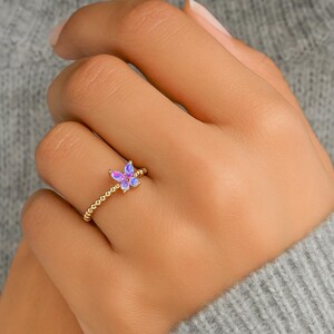 Puede incluir: Un anillo dorado con un dise&ntilde;o de mariposa con acentos iridiscentes morados y azules. La banda del anillo tiene una textura de cuentas. La mariposa es el punto focal, agregando un toque de fantas&iacute;a a la joyer&iacute;a.