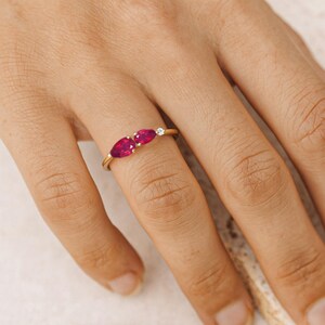 K&ouml;nnte beinhalten: Ein goldener Ring mit zwei oval geschliffenen, leuchtend roten Edelsteinen und einem kleinen, klaren Akzentstein. Der Ring ist auf einem zarten Goldband gefasst, das die Farbe und das Funkeln der Edelsteine hervorhebt. Ein Schmuckst&uuml;ck.