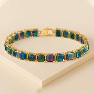 May include: A gold bracelet featuring rectangular, iridescent gemstones. The gemstones display a mix of blue, green, and purple hues. The bracelet is set in a gold metal frame and has a secure clasp.