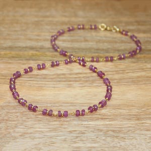 May include: A delicate necklace featuring small, faceted, deep pink gemstone beads interspersed with tiny gold-toned metal spacers. The beads are strung on a thin gold-toned wire, and the necklace includes a small gold-toned metal clasp closure.