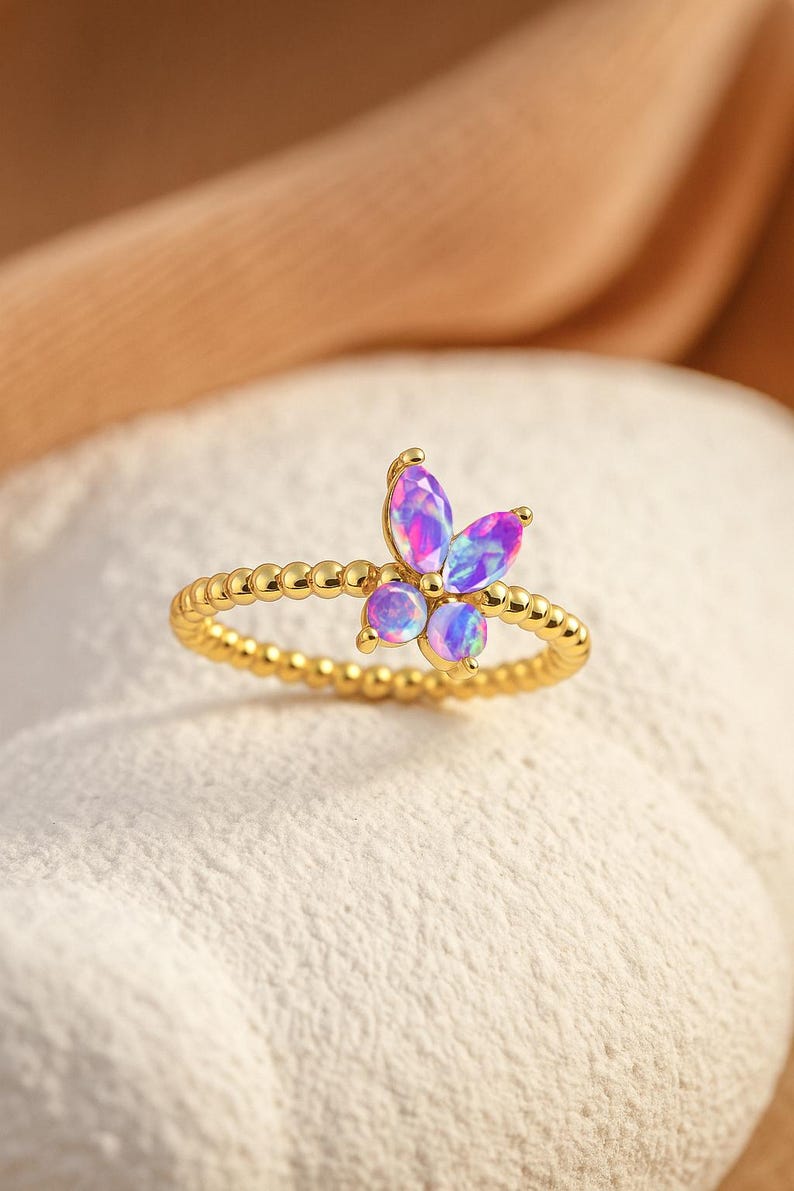 Puede incluir: Anillo dorado con dise&ntilde;o de mariposa con piedras preciosas iridiscentes moradas y azules. La banda del anillo tiene una textura de cuentas. La mariposa tiene tres piedras redondas y tres piedras en forma de marquesa.