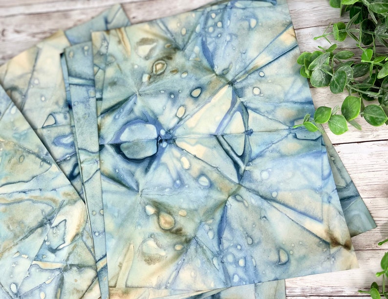 May include: A stack of blue and white patterned fabric squares with a subtle watercolour effect. The fabric has a crinkled texture and appears to be handmade.