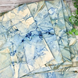 May include: A stack of blue and white marbled paper sheets. The paper has a unique, abstract pattern with shades of blue and white.