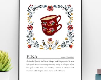 May include: A framed print featuring the word "FIKA" with a definition. The print showcases two red coffee cups with floral designs, surrounded by a floral border. The print is displayed on a white shelf with two potted succulents.