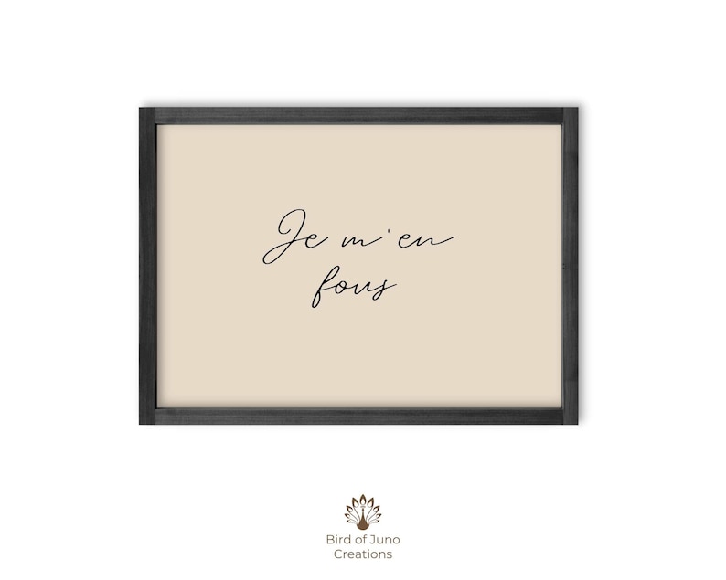 May include: A framed art print with the phrase "Je m'en fous" in elegant black script on a beige background. The frame is a simple, dark gray color. The print is a decorative piece.