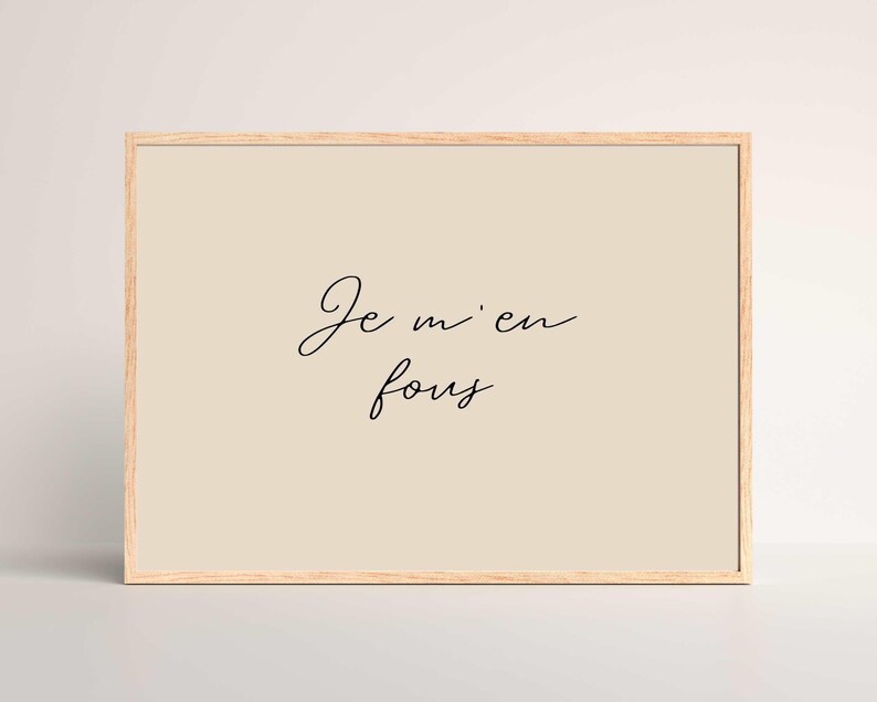 May include: A framed print with the phrase "Je m'en fous" in elegant black script on a beige background. The frame is a light wood color, and the overall aesthetic is minimalist and modern.