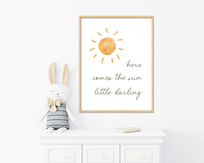 May include: A framed print with a watercolor illustration of a yellow sun and the text 'here comes the sun little darling'.