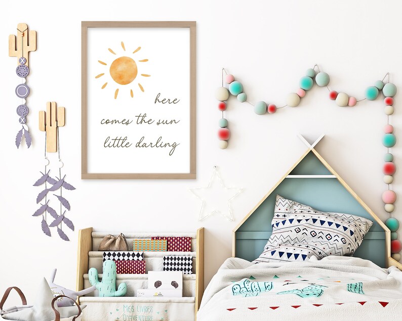 May include: A framed print with a watercolor sun illustration and the text "here comes the sun little darling." The room features a wooden bookshelf, a teepee-shaped bed frame, and decorative cactus wall hangings.