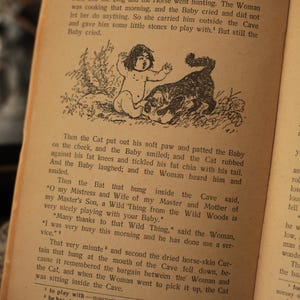 May include: A black and white illustration from a children's book depicting a cat comforting a crying baby. The text reads "Then the Cat put out his soft paw and patted the Baby on the cheek, and the Baby smiled; and the Cat rubbed against his fat knees and tickled his fat chin with his tail. And the Baby laughed; and the Woman heard him and smiled."