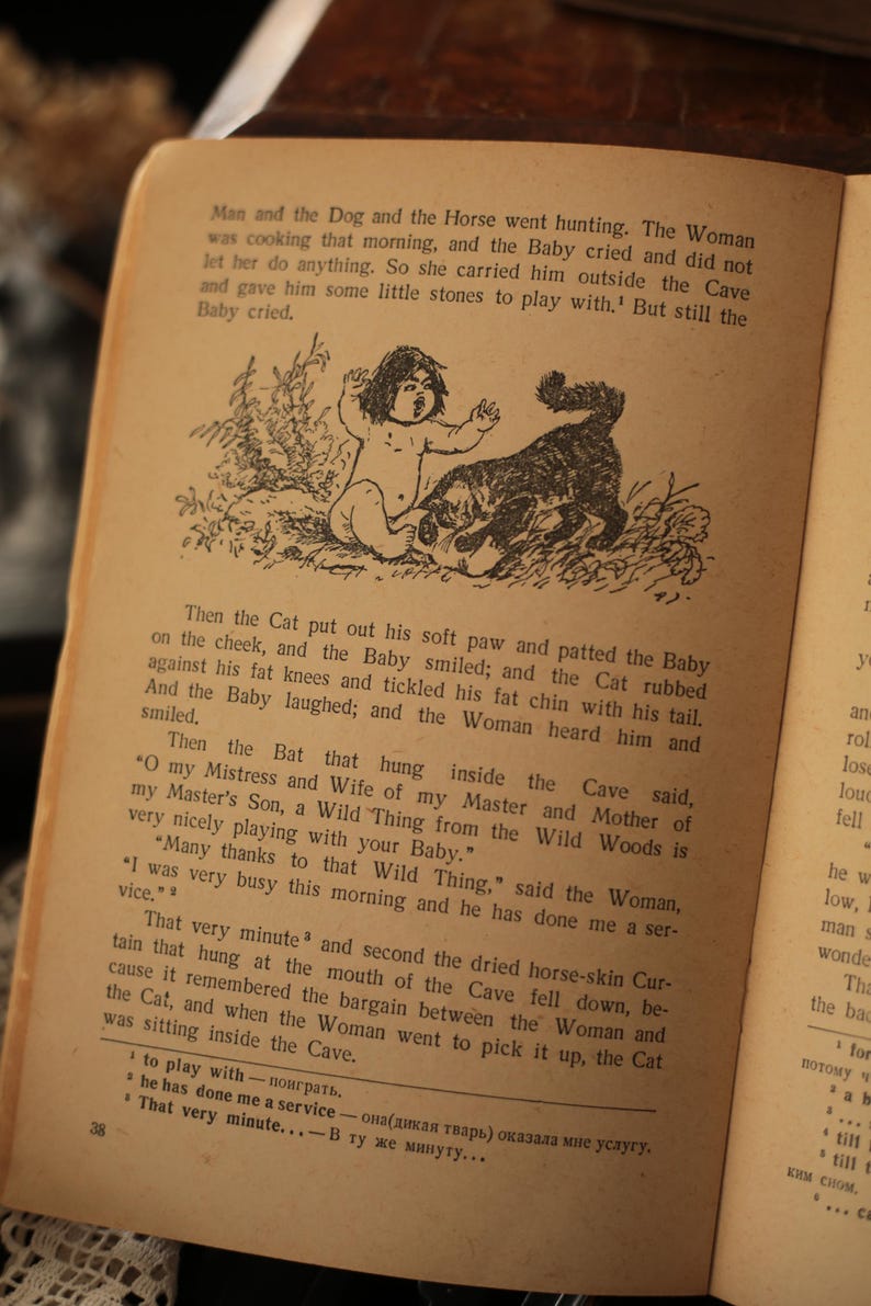 May include: A black and white illustration from a children's book depicting a cat comforting a crying baby. The text reads "Then the Cat put out his soft paw and patted the Baby on the cheek, and the Baby smiled; and the Cat rubbed against his fat knees and tickled his fat chin with his tail. And the Baby laughed; and the Woman heard him and smiled."