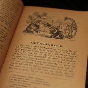 May include: An open book with a black and white illustration of an elephant with a trunk and other animals. The text on the page reads "THE ELEPHANT'S CHILD".