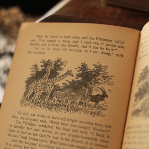 May include: An open book with black and white illustrations of animals. The text reads, "The te been a loud noise, and the Ethioplan called out, "I've caught a thing that I can't see. It smells like Giraffe, but it has no form. "Get on it's head till morning as I am doing," said the Leopard"