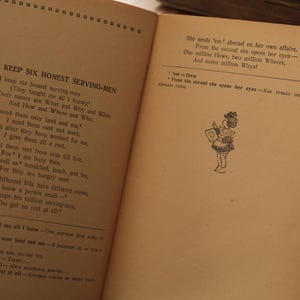 May include: A vintage book with a black and white illustration of a girl holding a book. The text on the page reads "I keep six honest serving-men" and "She sends 'em' abroad on her own affairs, From the second she opens her eyes - One million Hows, two million Wheres, And seven million Why's".