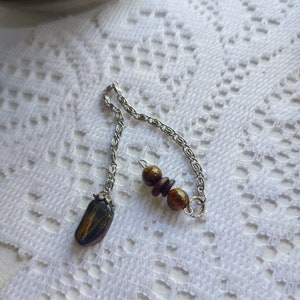 May include: A silver chain pendulum with a brown and black tiger's eye stone and three brown beads.